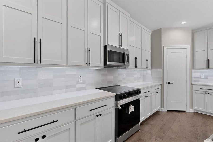 Kitchen featuring black / electric stove, backsplash, white cabinetry, stainless steel microwave, and recessed lighting Kitchen featuring black / electric stove, backsplash, white cabinetry, stainless steel microwave, and recessed lighting