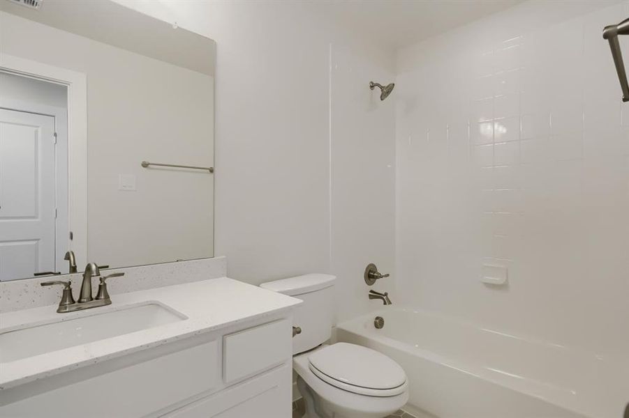 Bathroom featuring a white vanity with an integrated sink, a speckled light-toned countertop, a frameless wall mirror, and a white bathtub with a tiled surround
