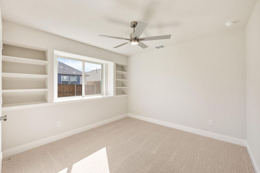 Empty bedroom with built-in shelves, ceiling fan, carpet flooring, and a large window Empty bedroom with built-in shelves, ceiling fan, carpet flooring, and a large window