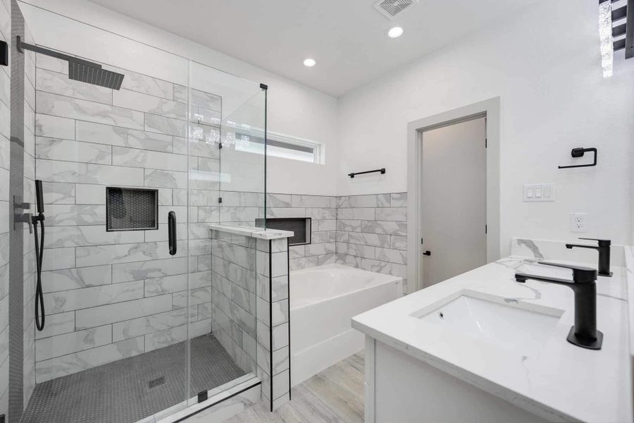 Spa-inspired primary bath featuring a large walk-in shower with rainfall showerhead, frameless glass enclosure, and a soaking tub with stylish tile surround and built-in niches.