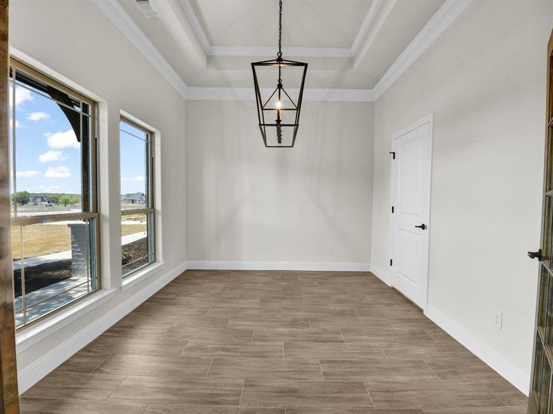 Unfurnished dining area featuring visible vents, crown molding, baseboards, wood tiled floor, and a tray ceiling Unfurnished dining area featuring visible vents, crown molding, baseboards, wood tiled floor, and a tray ceiling