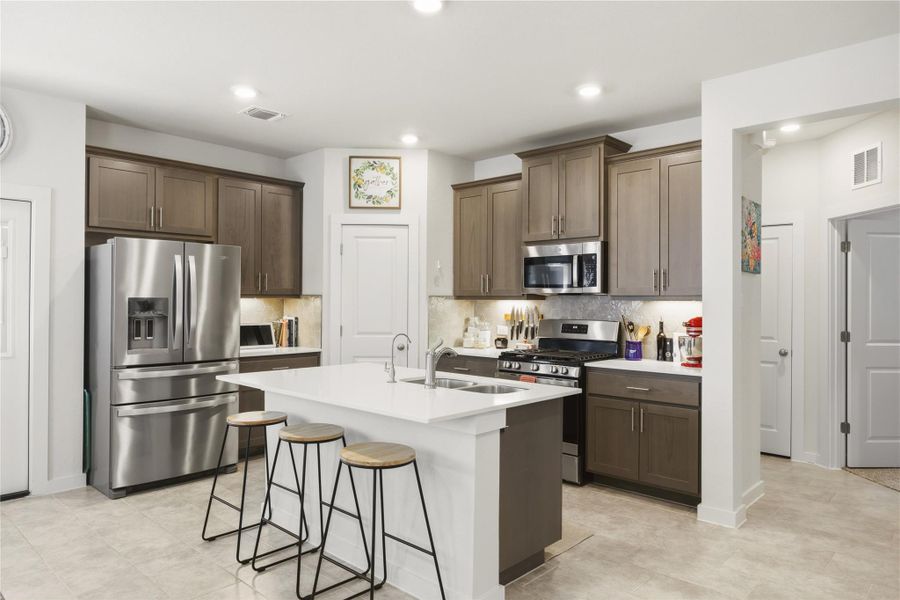 Kitchen with stainless steel appliances, an island with sink, a kitchen breakfast bar, tasteful backsplash, and dark wood finish cabinets