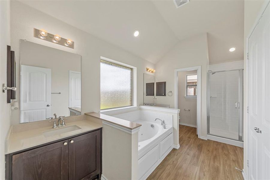 Bathroom with a stall shower, vaulted ceiling, a garden tub, vanity, and wood finished floors Bathroom with a stall shower, vaulted ceiling, a garden tub, vanity, and wood finished floors