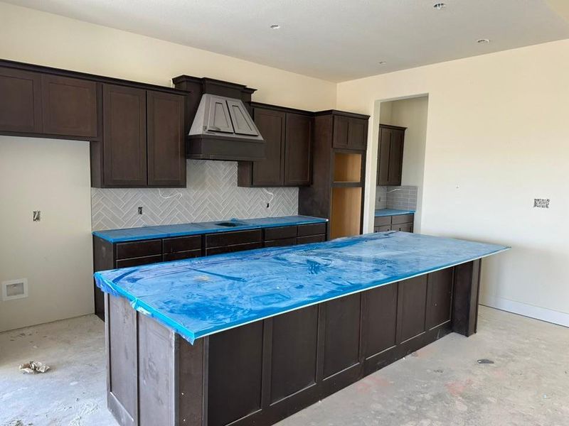 Spacious kitchen featuring dark wood cabinetry, a large center island with countertop, and a herringbone pattern tile backsplash