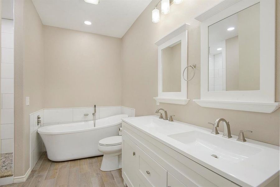 Full bathroom with wood finished floors, a freestanding bath, double vanity, and recessed lighting