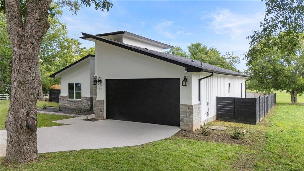 View of side of home with stone siding, driveway, a garage, and stucco siding View of side of home with stone siding, driveway, a garage, and stucco siding