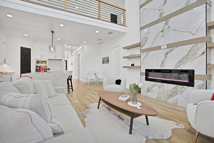 Living room featuring a towering ceiling, a high end fireplace, light hardwood / wood-style floors, and a notable chandelier