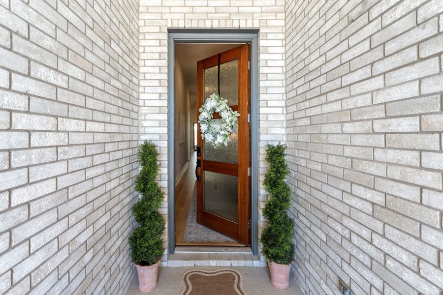 Entryway featuring a solid wood door with frosted glass panels, light-colored brick exterior, and a concrete porch