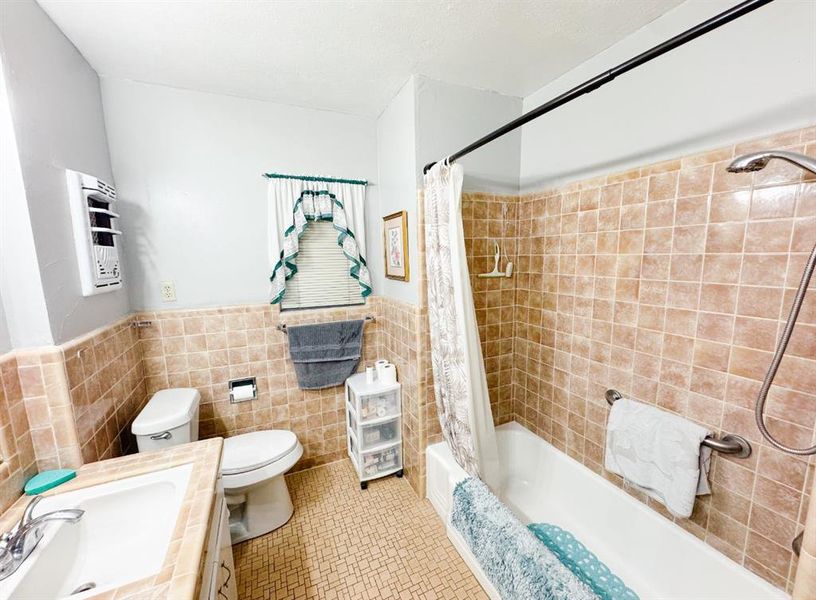 Full bathroom featuring tile walls, shower / bath combo with shower curtain, a wainscoted wall, tile patterned flooring, and vanity