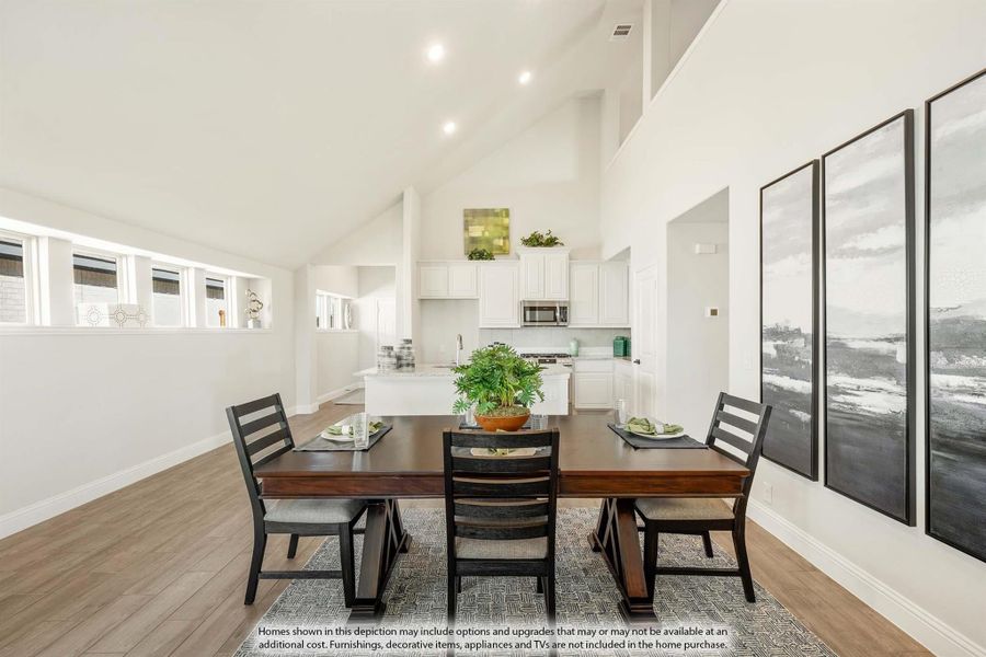 Dining area with dark wood table, four chairs, and open kitchen with white cabinets and high vaulted ceiling