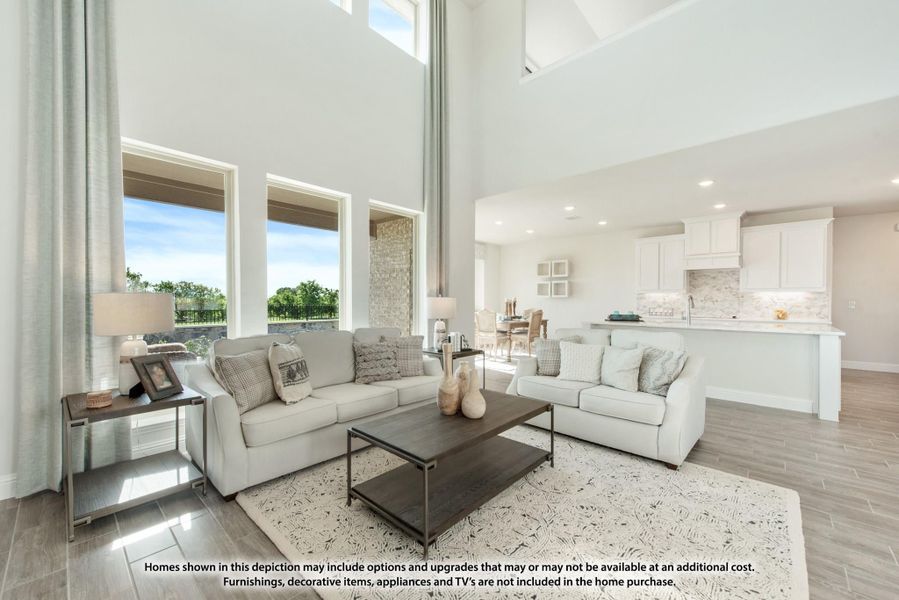 Open-concept living room with two-story ceiling, large windows, and view into kitchen and dining area