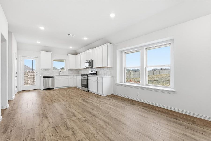 Kitchen with stainless steel appliances, white cabinetry, light countertops, light wood finished floors, and recessed lighting