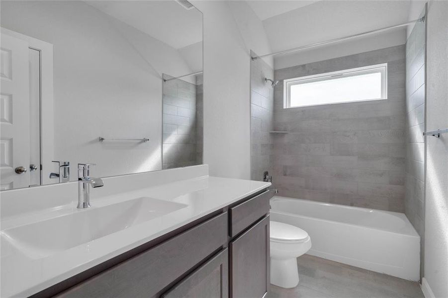 Secondary bathroom features light countertops and grey cabinets, neutral paint, shower/tub combo with tile surround, large mirror, tile floors, sleek fixtures and modern finishes, plenty of space to accommodate any visiting family or guests.