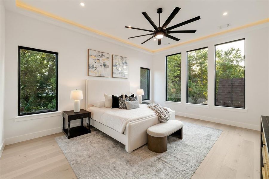 Bright interior space with light wood-finish flooring, featuring four tall windows with black frames, a contemporary ceiling fan, and recessed lighting with perimeter accent lighting Bright interior space with light wood-finish flooring, featuring four tall windows with black frames, a contemporary ceiling fan, and recessed lighting with perimeter accent lighting