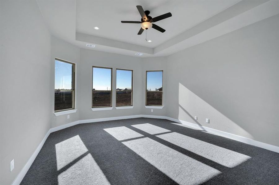 Carpeted empty room with ceiling fan and a raised ceiling