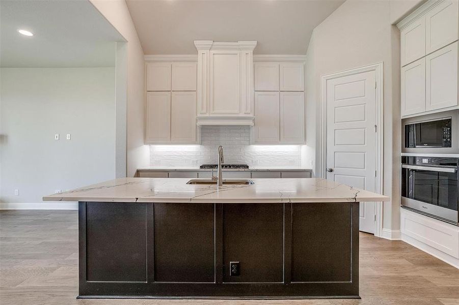 Kitchen featuring white cabinets, an island with sink, appliances with stainless steel finishes, and light hardwood / wood-style flooring