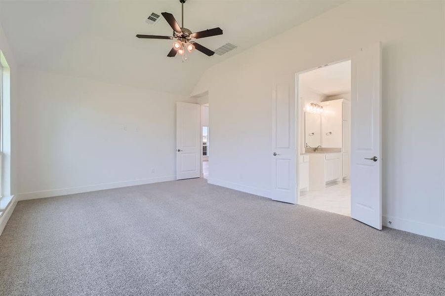 Unfurnished bedroom with connected bathroom, ceiling fan, light carpet, and lofted ceiling