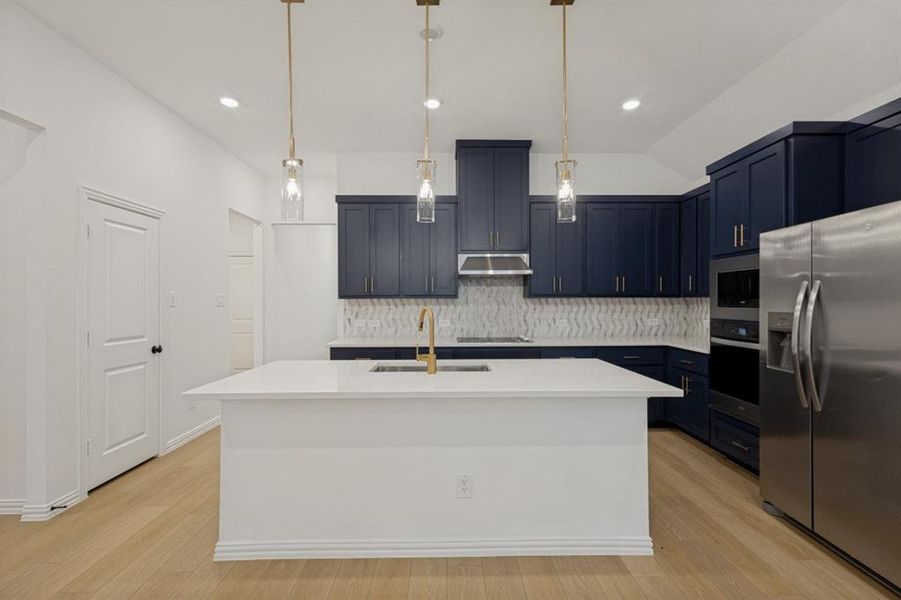 Contemporary kitchen featuring a large central island with a solid surface countertop, dark blue cabinetry, wood-finish flooring, stainless steel appliances, and pendant lighting