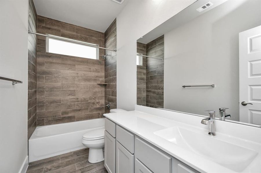 Secondary bath features tile flooring, bath/shower combo with tile surround, light stained wood cabinets, beautiful light countertop, and modern harware. Sample photo of completed home with similar plan. As built color and selections will vary.