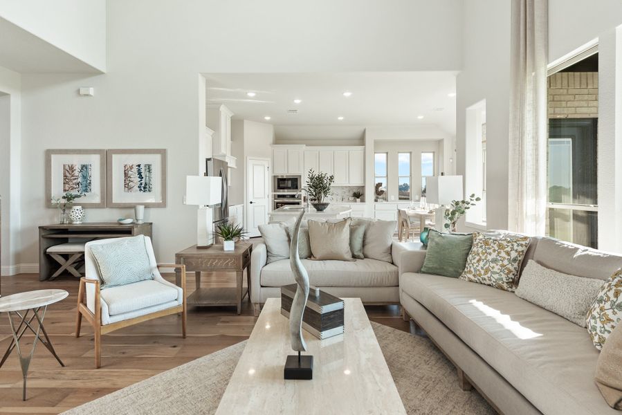 Open-concept living room with high ceilings, neutral sofas, and kitchen visible in background