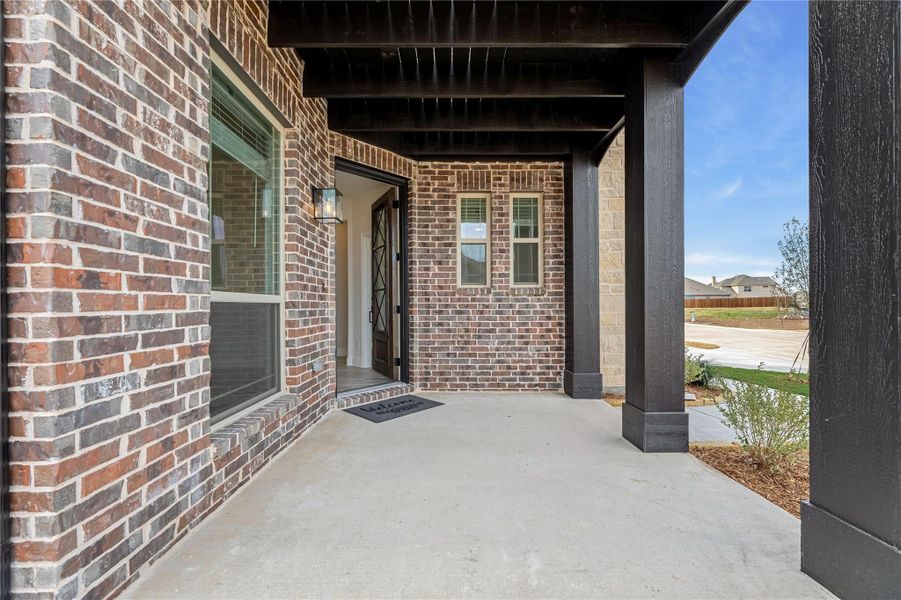 Covered front porch with brick exterior, dark columns, and glass-panel front door with wall sconce Covered front porch with brick exterior, dark columns, and glass-panel front door with wall sconce