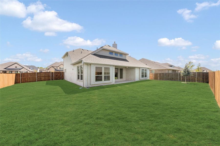 Backyard of brick home with large green lawn, covered patio, and wood privacy fence