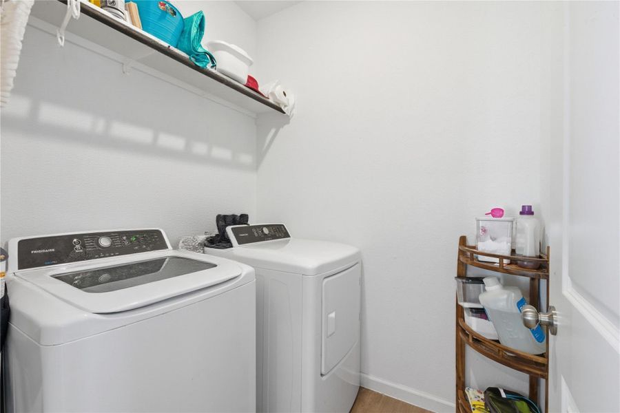 This photo shows a compact, well-organized laundry room with a washer and dryer set, a wall-mounted shelf for storage.