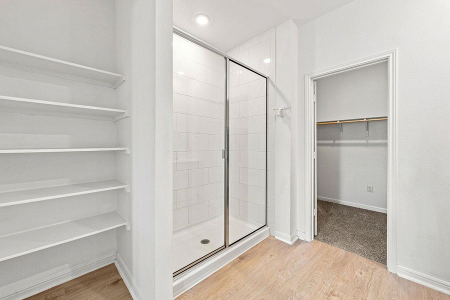 A glass-enclosed shower stall sits adjacent to a walk-in closet and built-in shelving.