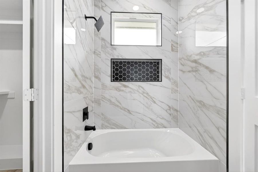 Bathtub and shower combination featuring white marble-look wall tiling, a black hexagonal tile niche, and matte black fixtures Bathtub and shower combination featuring white marble-look wall tiling, a black hexagonal tile niche, and matte black fixtures