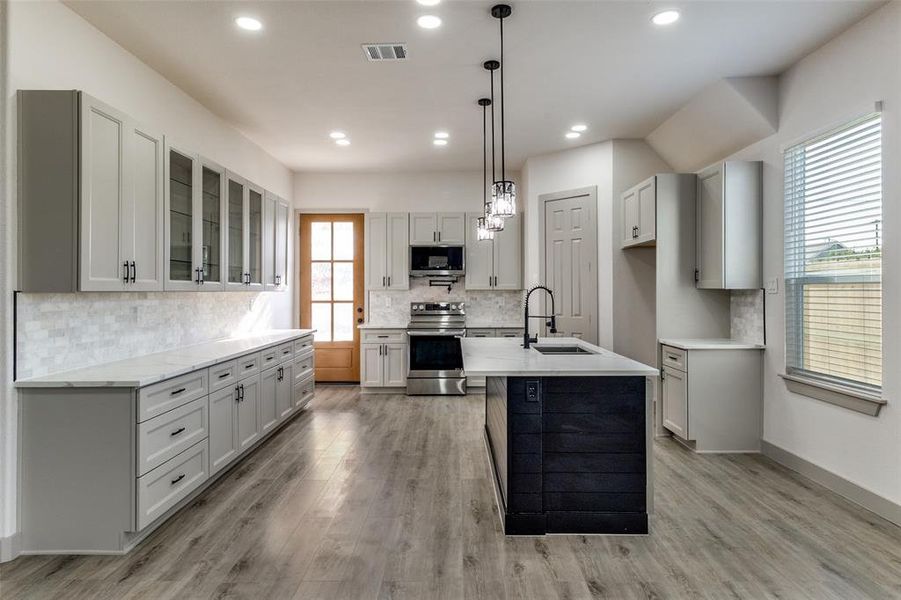 Kitchen featuring a center island with sink, decorative light fixtures, stainless steel appliances, light wood-style floors, and backsplash Kitchen featuring a center island with sink, decorative light fixtures, stainless steel appliances, light wood-style floors, and backsplash