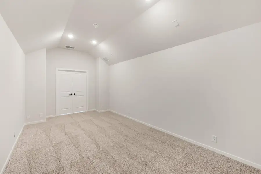 Empty bedroom with vaulted ceiling, beige carpet, and white double doors