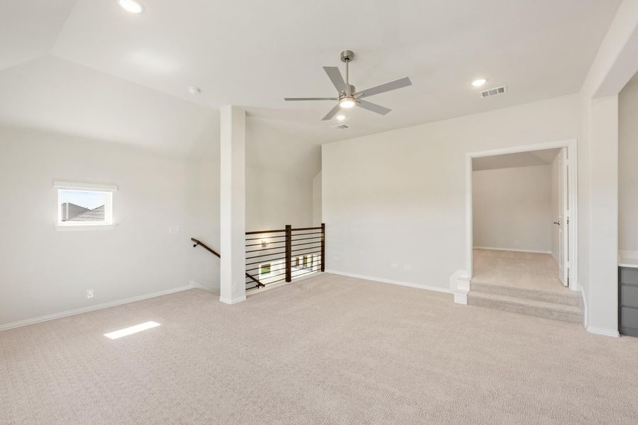 Open upstairs loft with carpet, ceiling fan, stair railing, and doorway to adjoining room Open upstairs loft with carpet, ceiling fan, stair railing, and doorway to adjoining room