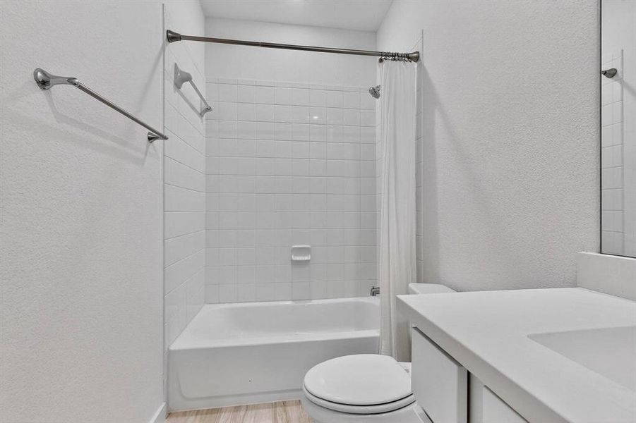 Full bathroom featuring a textured wall, shower / bath combo with shower curtain, vanity, and light wood-type flooring Full bathroom featuring a textured wall, shower / bath combo with shower curtain, vanity, and light wood-type flooring