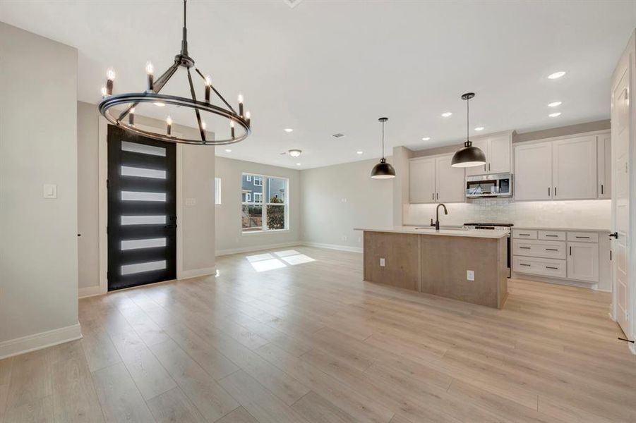 Kitchen with open floor plan, a kitchen island with sink, stainless steel microwave, backsplash, and suspended lighting