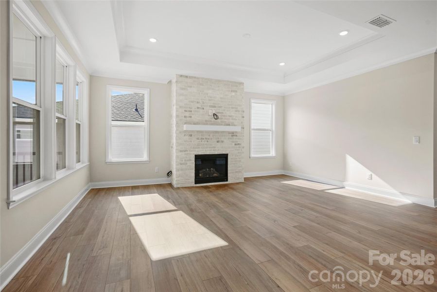 Inviting gas fireplace, tray ceiling, crown molding, and large windows enhance gathering room