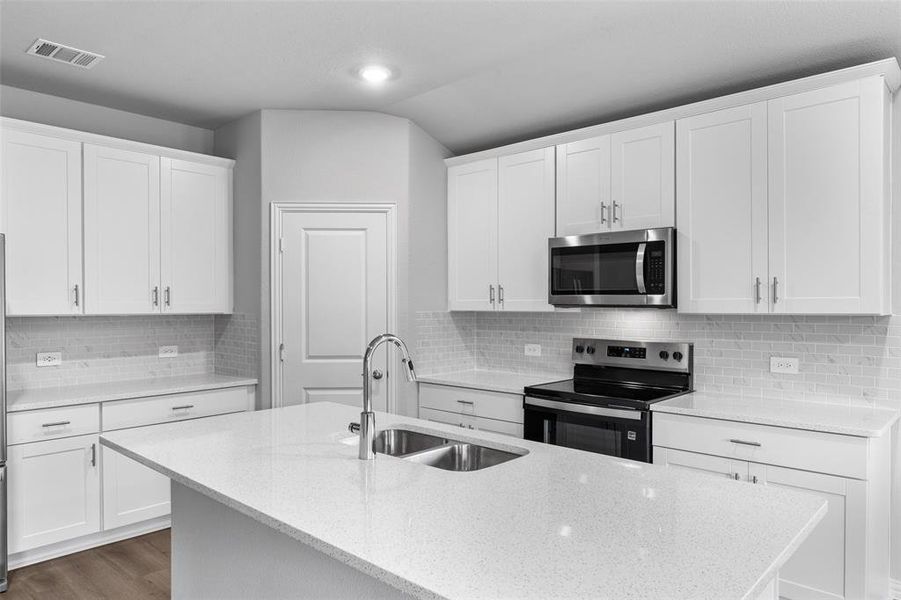 Kitchen featuring appliances with stainless steel finishes, a kitchen island with sink, light stone counters, vaulted ceiling, and white cabinetry Kitchen featuring appliances with stainless steel finishes, a kitchen island with sink, light stone counters, vaulted ceiling, and white cabinetry