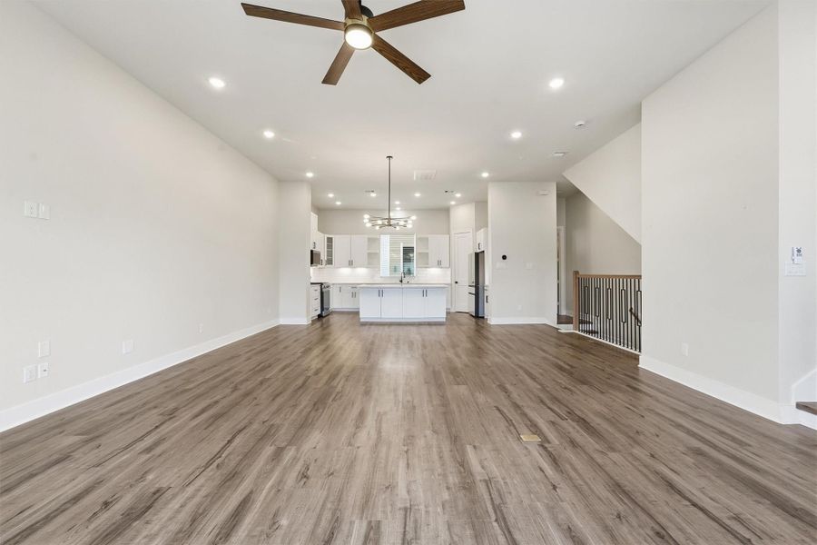 Spacious open-concept living and kitchen area featuring wide-plank flooring, a large island, modern ceiling fan, recessed lighting, and sleek contemporary finishes throughout.