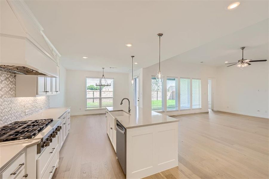 Kitchen with light hardwood / wood-style floors, tasteful backsplash, a kitchen island with sink, white cabinetry, and appliances with stainless steel finishes