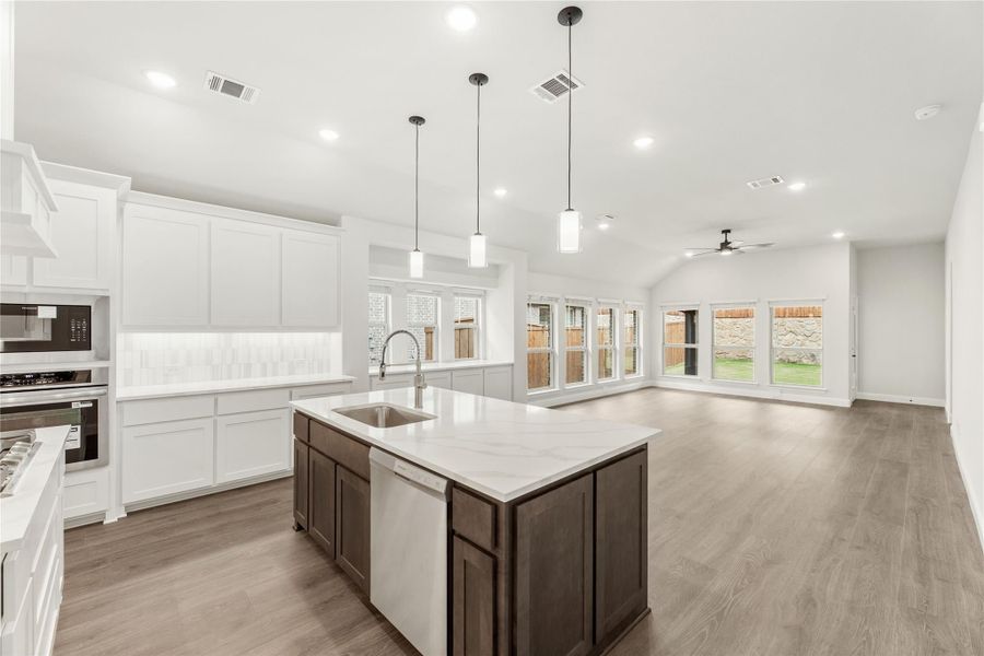 Open kitchen with large island, white quartz countertops, dark cabinets, and pendant lights opening to living area with hardwood floors Open kitchen with large island, white quartz countertops, dark cabinets, and pendant lights opening to living area with hardwood floors