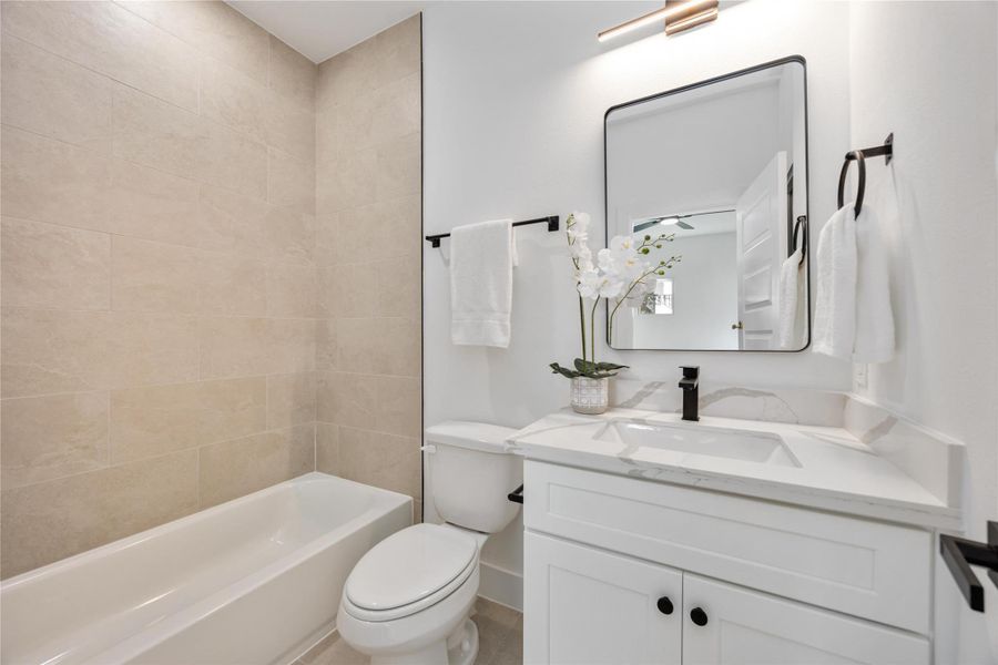 A bright, modern en suite bathroom features a clean white vanity, black hardware accents, and a tiled shower-tub combo for a sleek, minimalist look.