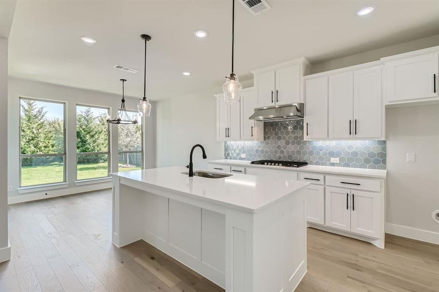 Kitchen with sink, hanging light fixtures, white cabinetry, light hardwood / wood-style floors, and a center island with sink