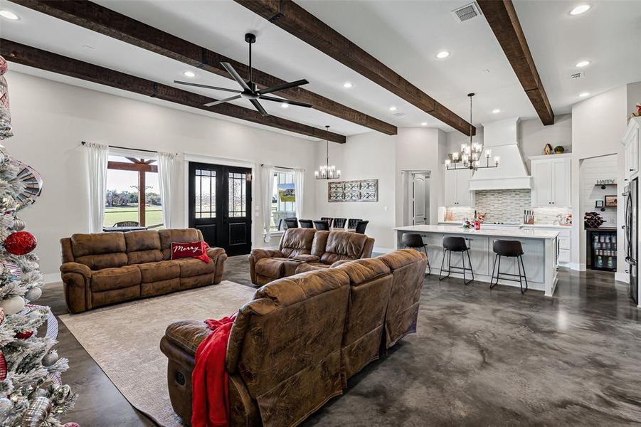 Living room with concrete floors, a chandelier, a ceiling fan, recessed lighting, and beamed ceiling Living room with concrete floors, a chandelier, a ceiling fan, recessed lighting, and beamed ceiling