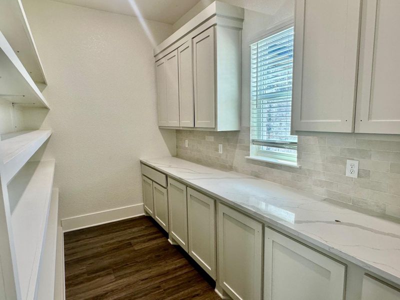 Kitchen featuring dark wood-style flooring, light stone countertops, white cabinetry, a textured wall, and backsplash