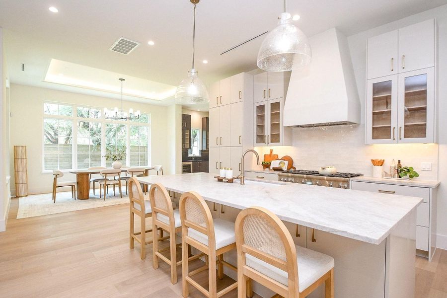 This bright, modern kitchen features a spacious island with seating, sleek white cabinetry, and stainless steel appliances. The open layout flows into a dining area with large windows, offering ample natural light and a view of the backyard.