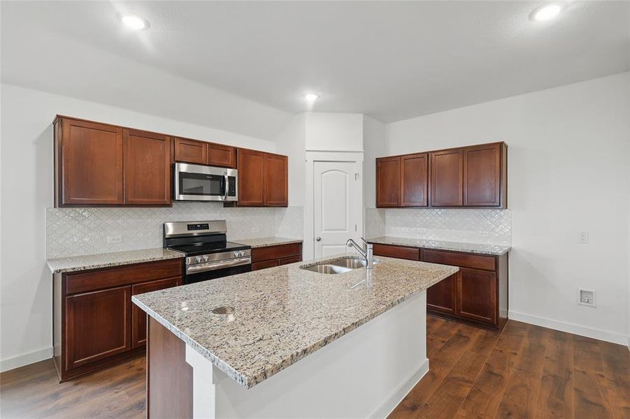 Kitchen with appliances with stainless steel finishes, light stone counters, dark wood-style floors, and decorative backsplash Kitchen with appliances with stainless steel finishes, light stone counters, dark wood-style floors, and decorative backsplash