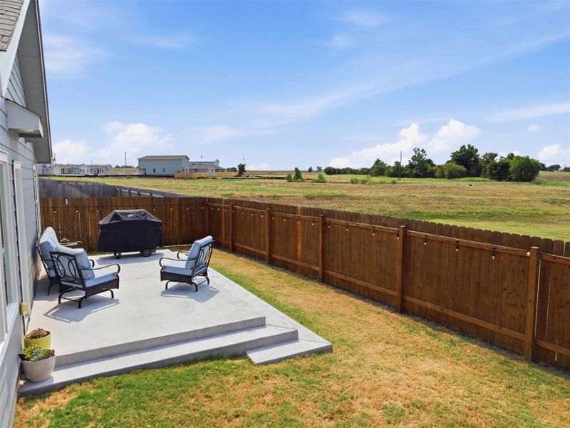 A concrete patio steps down to the grass yard bordered by a wooden privacy fence.