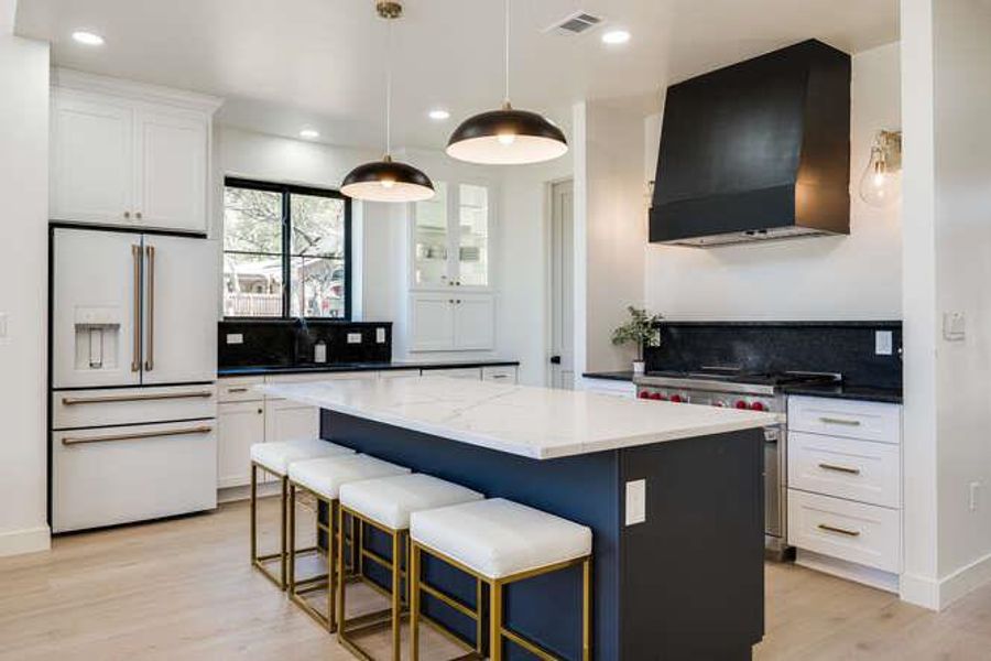 Kitchen with premium appliances, white cabinets, a kitchen breakfast bar, wall chimney exhaust hood, and recessed lighting