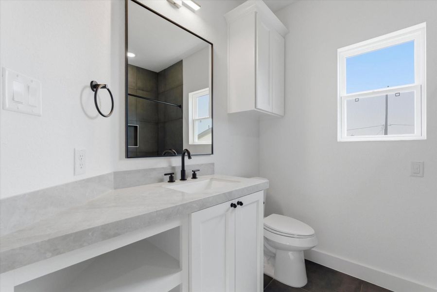 Another secondary bath upstairs features a functional vanity with extra storage and cabinetry, paired with a relaxing jetted shower-tub combo.