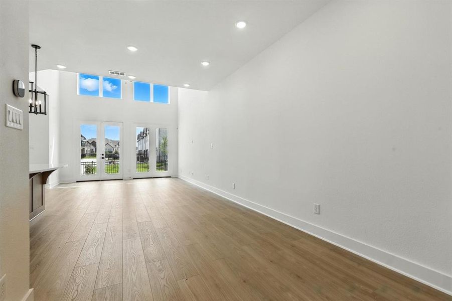 Unfurnished living room with french doors, recessed lighting, light wood-style floors, and a towering ceiling Unfurnished living room with french doors, recessed lighting, light wood-style floors, and a towering ceiling