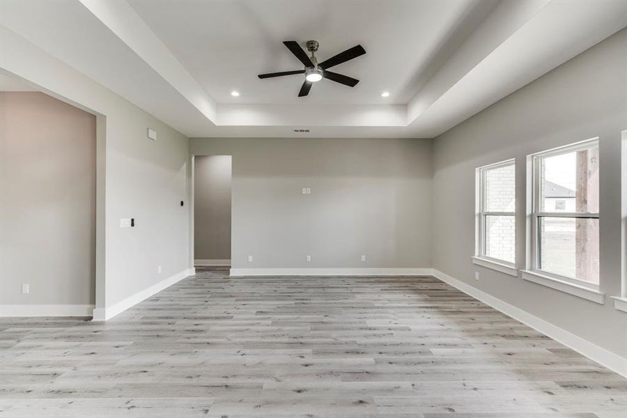 Unfurnished room with ceiling fan, light hardwood / wood-style flooring, and a tray ceiling